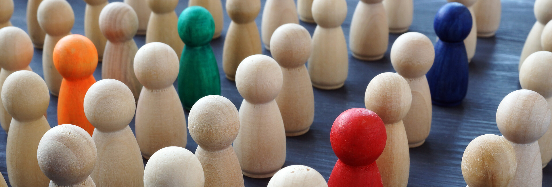 Gruppe von naturfarbenen Holzfiguren, in der 4 Figuren farbig hervorgehoben sind