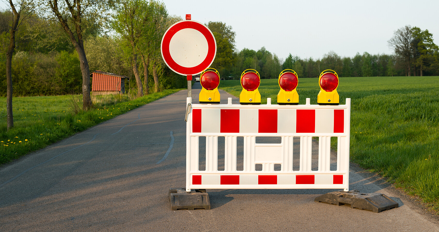 Strassenbarken und ein Schild sperren eine Straße auf dem Land ab. 