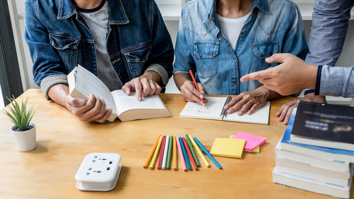 Lehramtsstuden*innen sitzen am Tisch und arbeiten zusammen - man sieht nur die Hände und die Arbeitsmaterialien auf dem Tisch