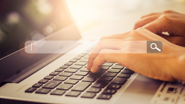 Frauenhände geben einen Suchbegriff auf dem Laptop ein