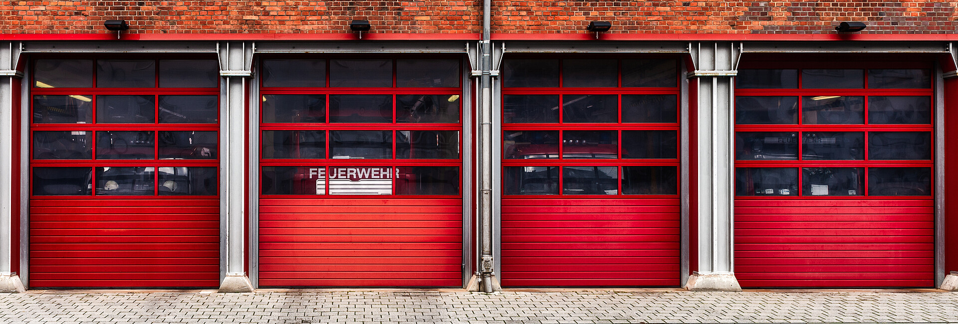 Bild zeigt ein Feuerwehrhaus, hinter dessen Fenster ein Feuerwehrfahrzeugt steht