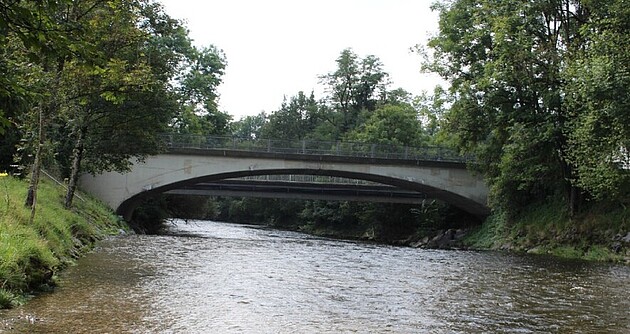 Man blickt auf eine Brücke, die über die Untere Argen führt; Im Hintergrund Bäume