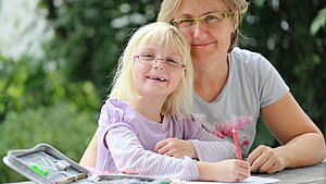 Mutter und Tochter sitzen gemeinsam an einem Tisch im Freien und machen Hausaufgaben