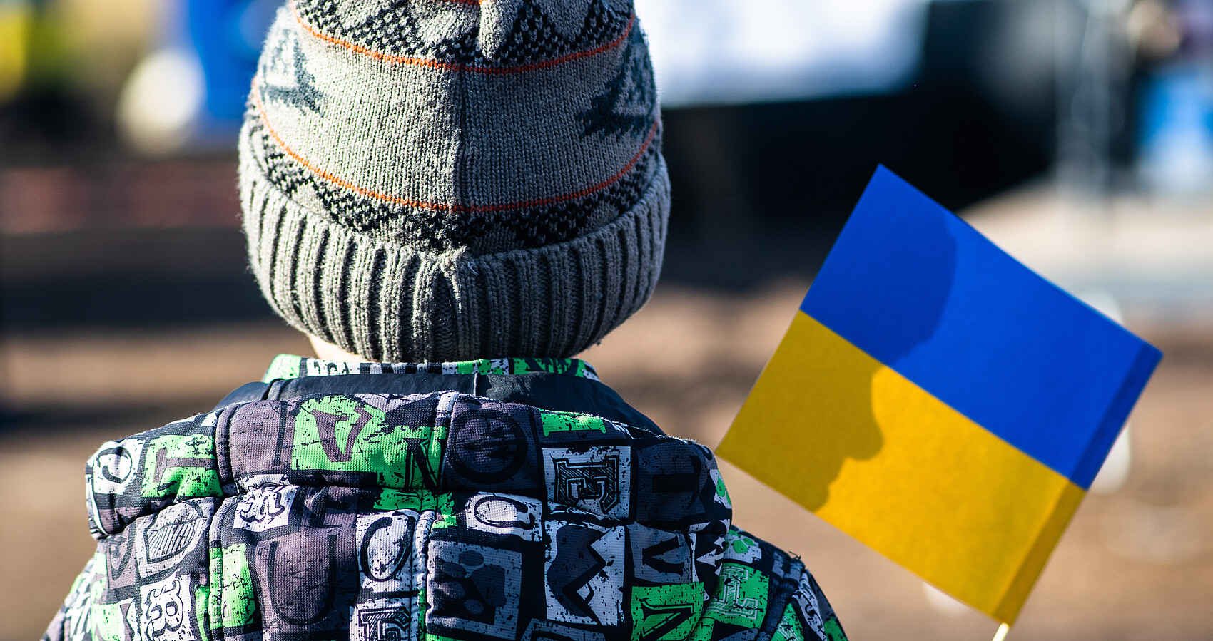 Bild zeigt ein Kind von hinten mit der ukrainischen Flagge in der Hand