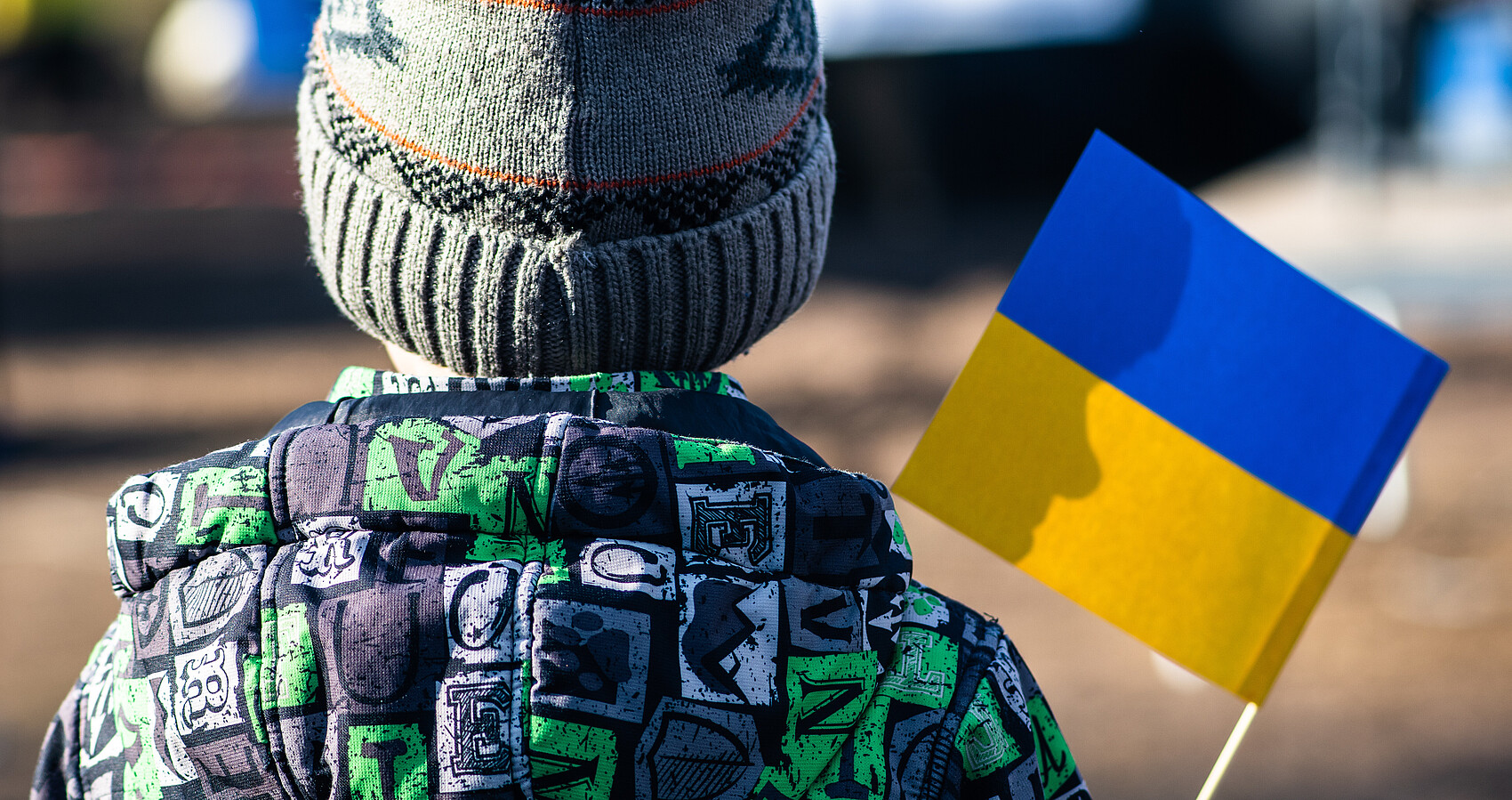 Bild zeigt ein Kind von hinten mit der ukrainischen Flagge in der Hand