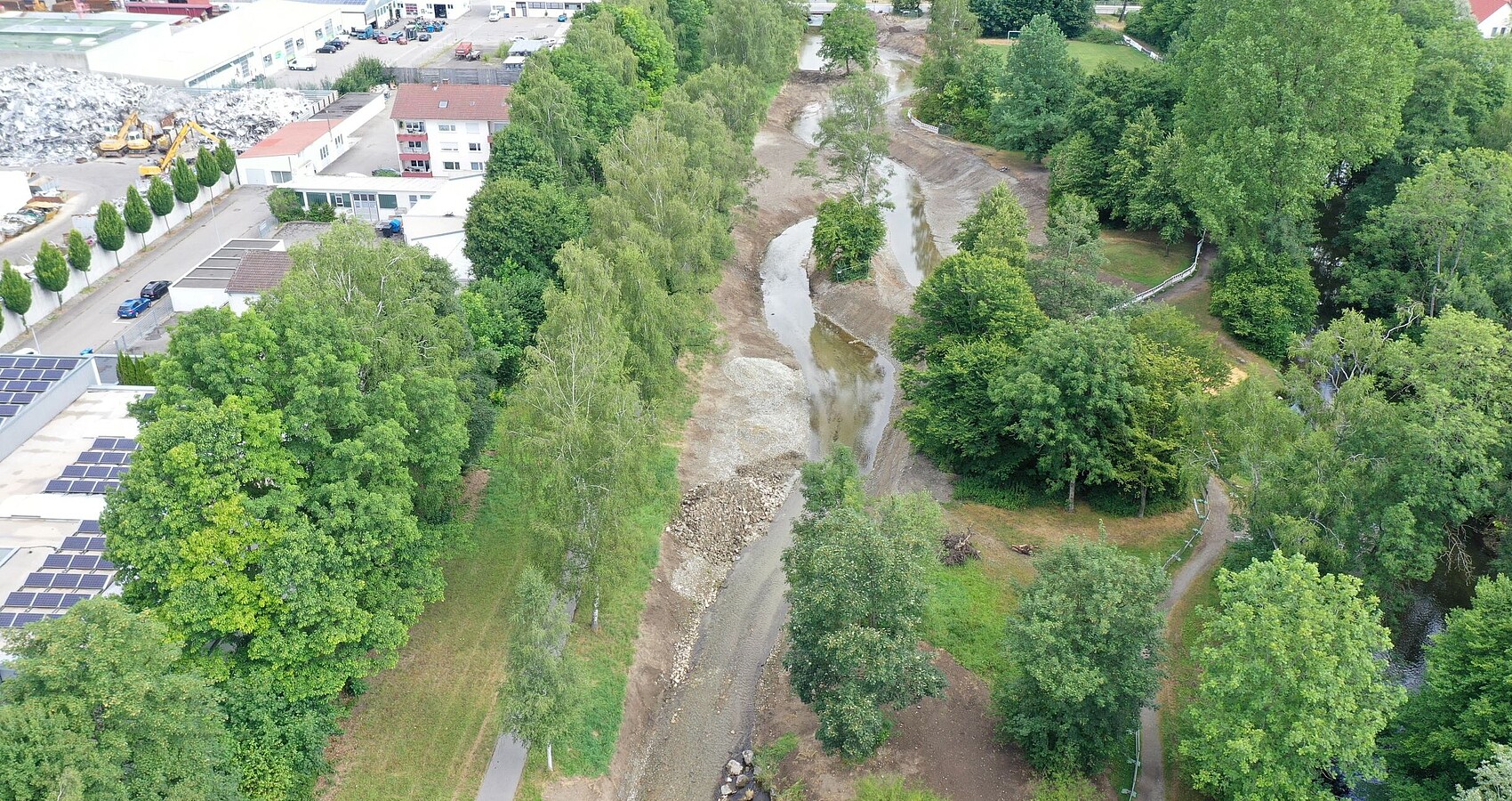 Das Bild zeigt einen revitalisierter Abschnitt der Riss bei Biberach; Bäume und Sträucher und Gebäude links