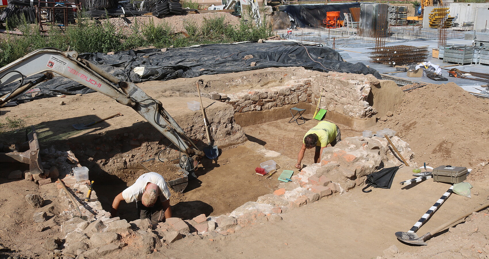 Bild zeigt wie Archäologen den Keller untersuchen, im Hingrund Bauarbeiten