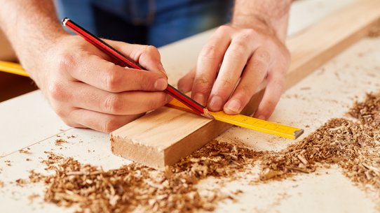 Ein Zollstock und ein Stück Holz, jemand zeichnet etwas ein