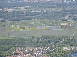 Luftbildaufnahme des Polder Rheinschanzinsel mit Blick in Richtung Norden. Zu sehen sind die mit Wasser gefüllten Gräben und Schluten im Bereich der Fläche für die partiellen Flutungen zur Auenrenaturierung. Im Hintergrund ist das überflutete Rheinvorland und auf der gegenüberliegenden Seite des Rheins der Polder Mechtersheim zu sehen.