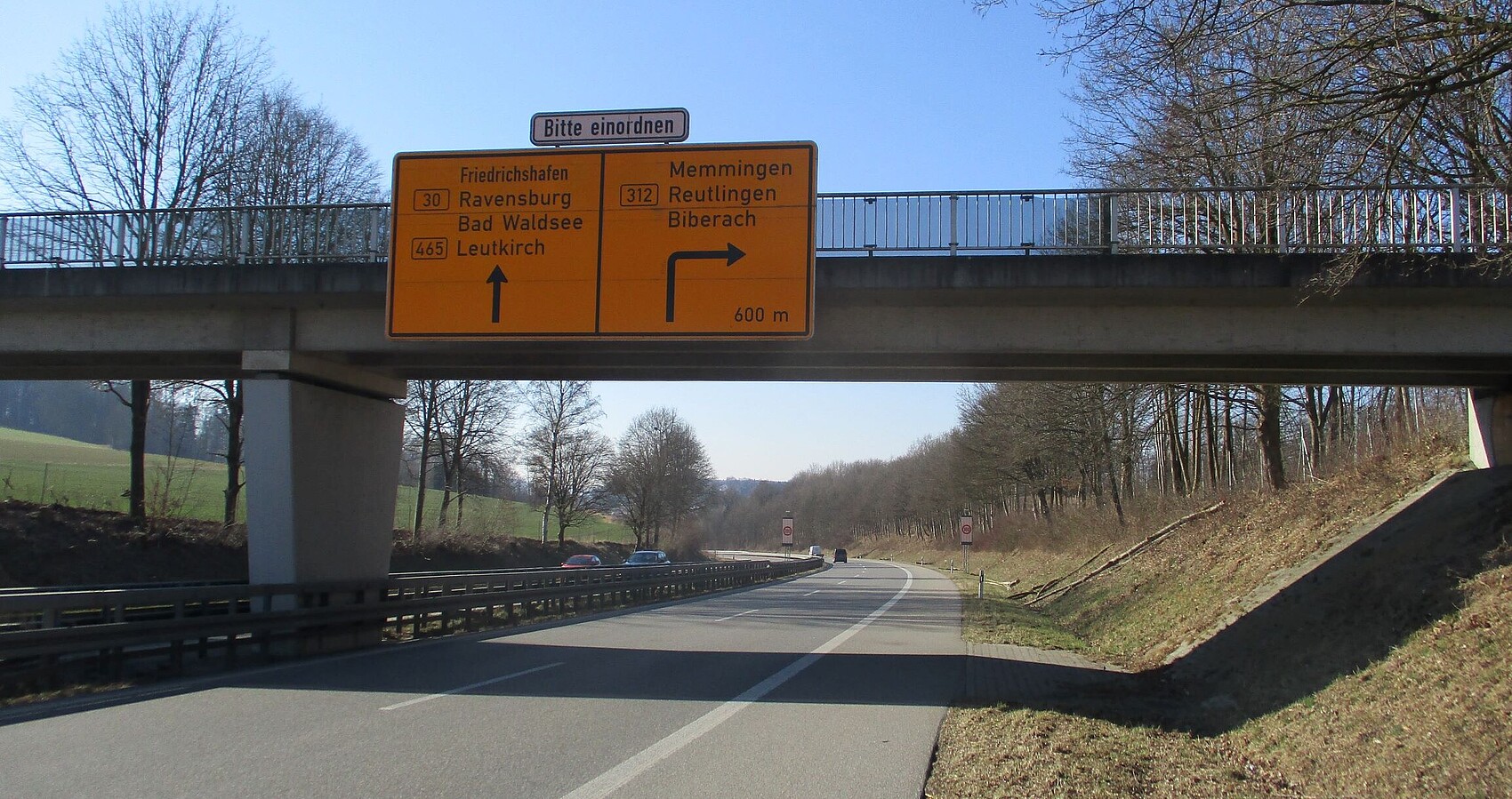 Man blickt auf eine Brücke an der Verkehrszeichen befestigt sind. Darunter verläuft die B 30 bei Biberach-Hagenbuch