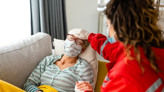 Eine Notfallsanitäterin versorgt eine im Bett liegende Frau