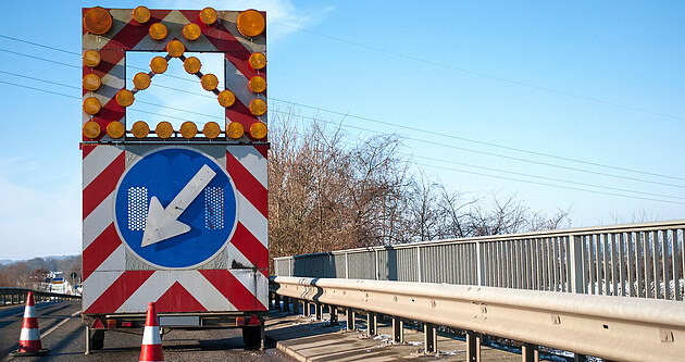 Blick auf eine Brücke auf der sich ein Baustellenfahrzeug mit einem Hinweisschild auf eine Fahrbahnverengung befindet