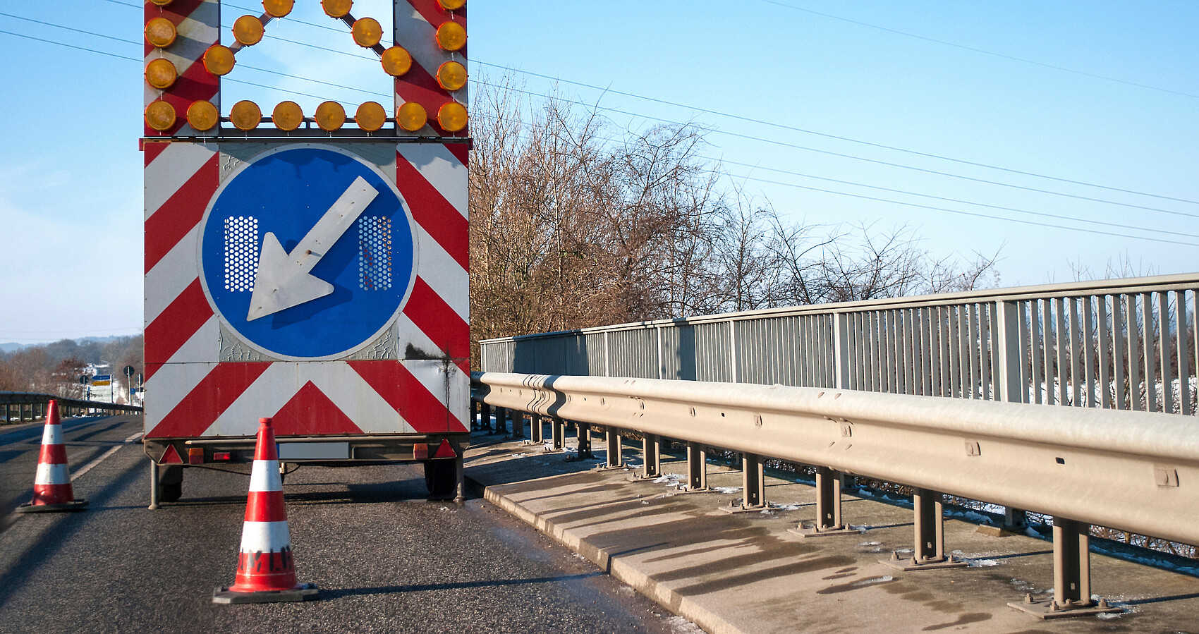 Blick auf eine Brücke auf der sich ein Baustellenfahrzeug mit einem Hinweisschild auf eine Fahrbahnverengung befindet