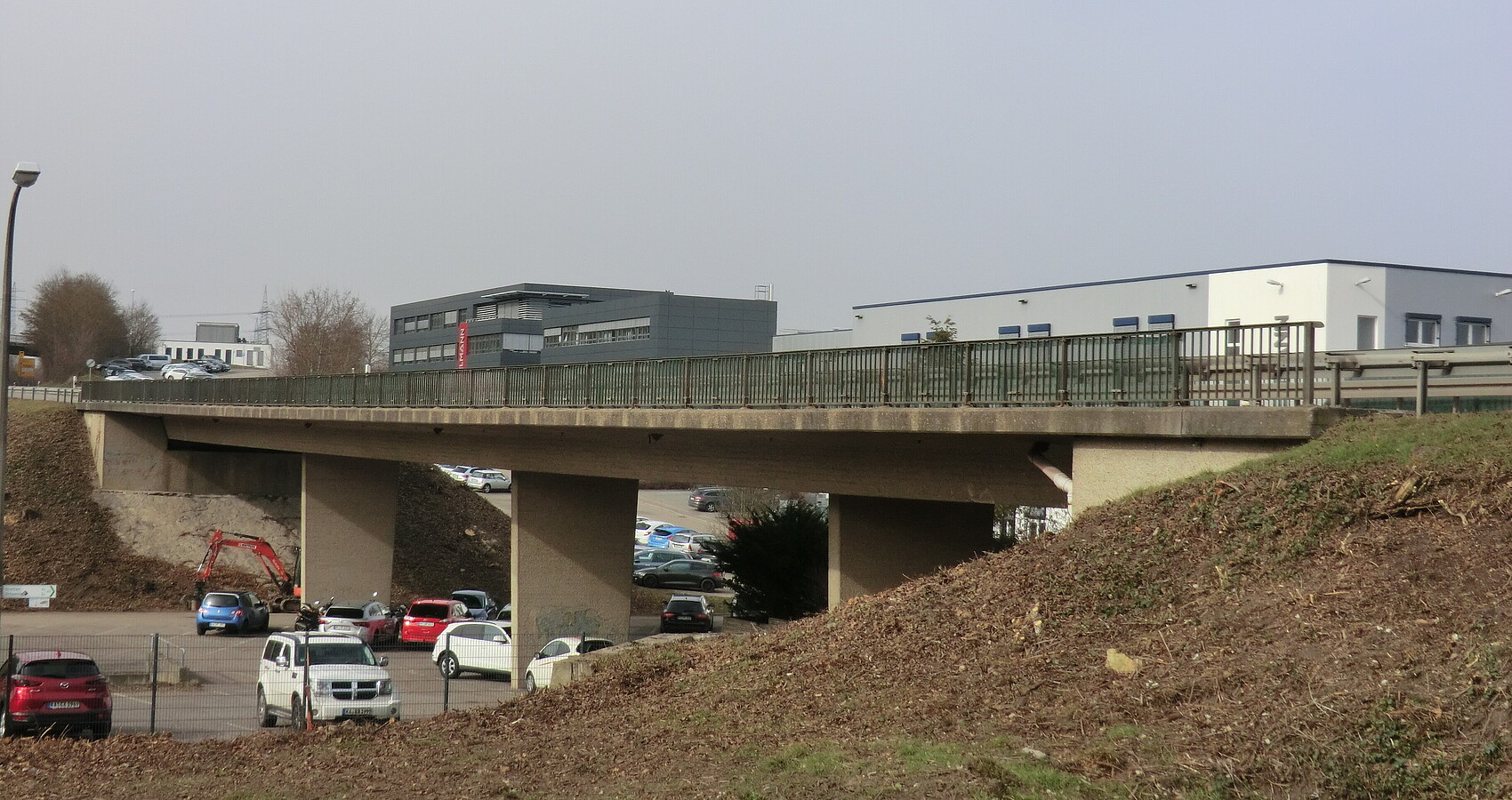 Bestehende Kieselmannbrücke über die K 4520 bei Knittlingen. Unterhalb der Brücke sind parkende Fahrzeuge zu sehen, im Hintergrund verschiedene Firmengebäude.