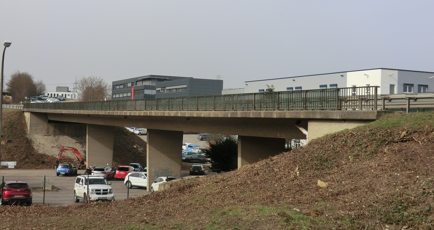 Bestehende Kieselmannbrücke über die K 4520 bei Knittlingen. Unterhalb der Brücke sind parkende Fahrzeuge zu sehen, im Hintergrund verschiedene Firmengebäude.