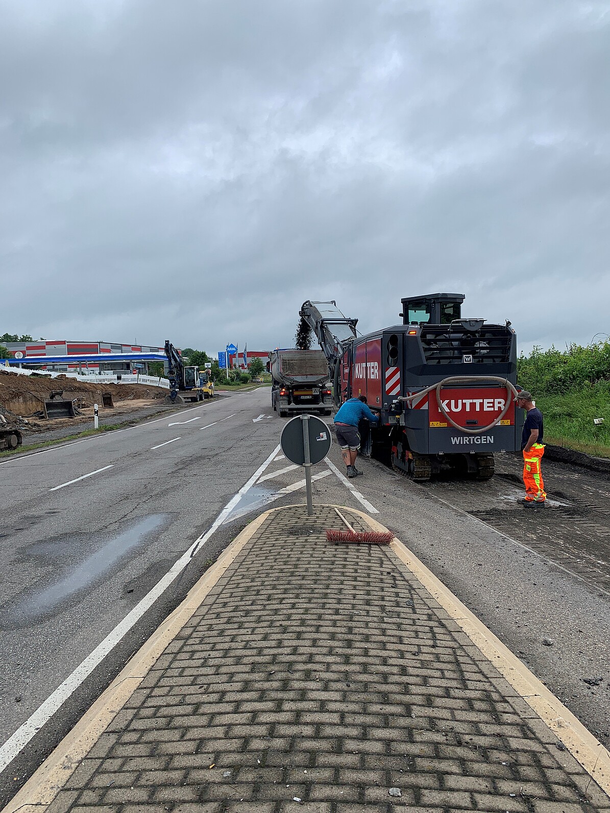 Baustellenfahrzeuge und zwei Arbeiter stehen am Fahrbahnrand