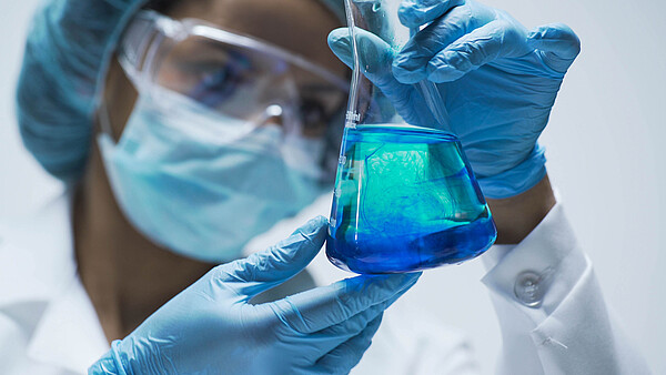 Wissenschaftlerin mit Glaskolben und einer blauen Lösung darin