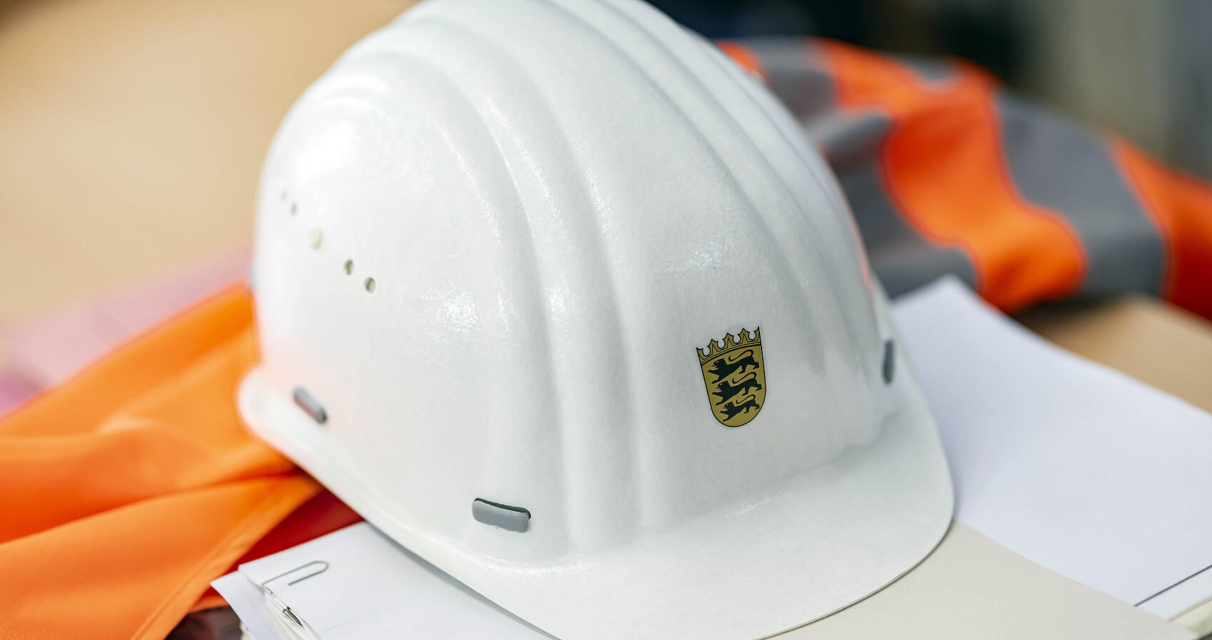 Auf einer Sicherheitsweste und auf einem Papierstapel liegt ein Bauhelm