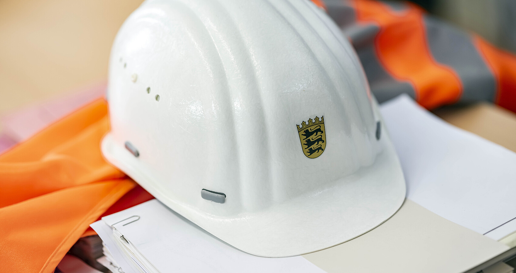 Auf einer Sicherheitsweste und auf einem Papierstapel liegt ein Bauhelm