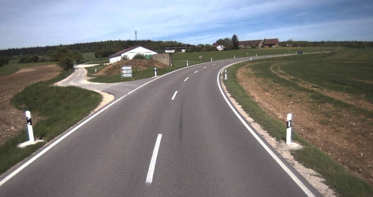 Das Foto zeigt eine neu asphaltierte und markierte einspurige Straße. Links ein Gebäude