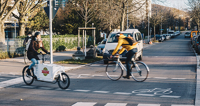 Bild zeigt 2 Fahrradfahrer beim Überqueren einer Straße