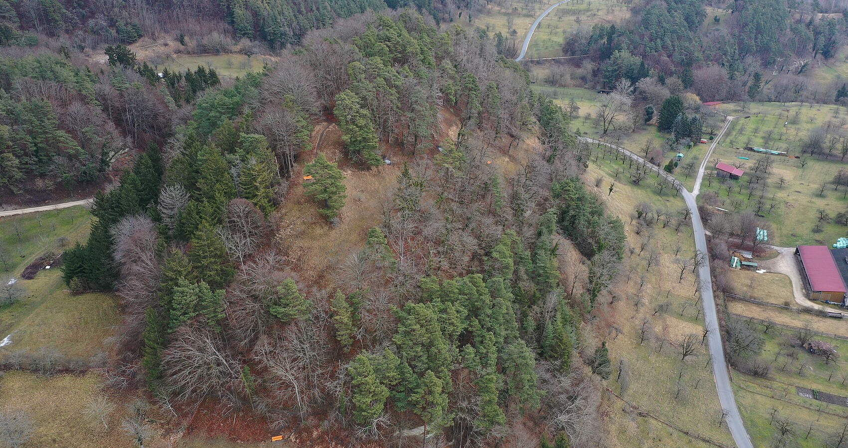 Das Foto zeigt das NSG Sipplinger Dreieck von oben. Hüglige bewaldete Landschaft. Waldweg. Eine Straße. vereinzelt Hütten und ein landwirtschaftliches Gebäude