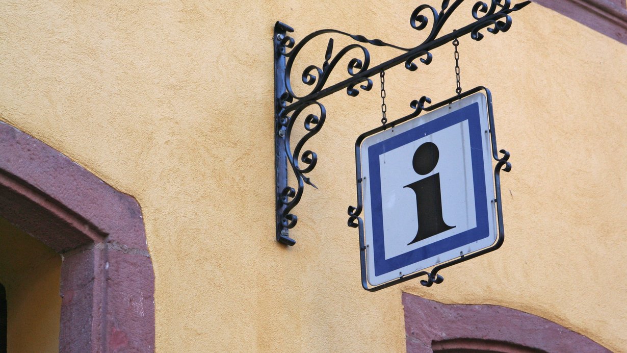 Schild mit dem Buchstaben "i" vor einer Touristikinformation 