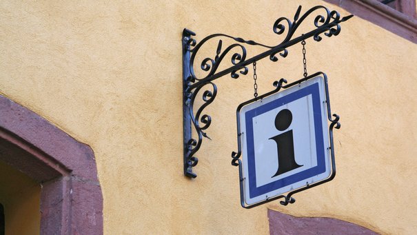 Schild mit dem Buchstaben "i" vor einer Touristikinformation 