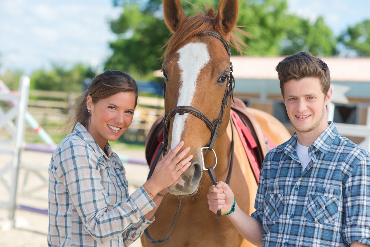 Praktikantin und Praktikant; zwischen beiden ein Pferd