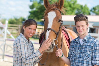 Praktikantin und Praktikant; zwischen beiden ein Pferd
