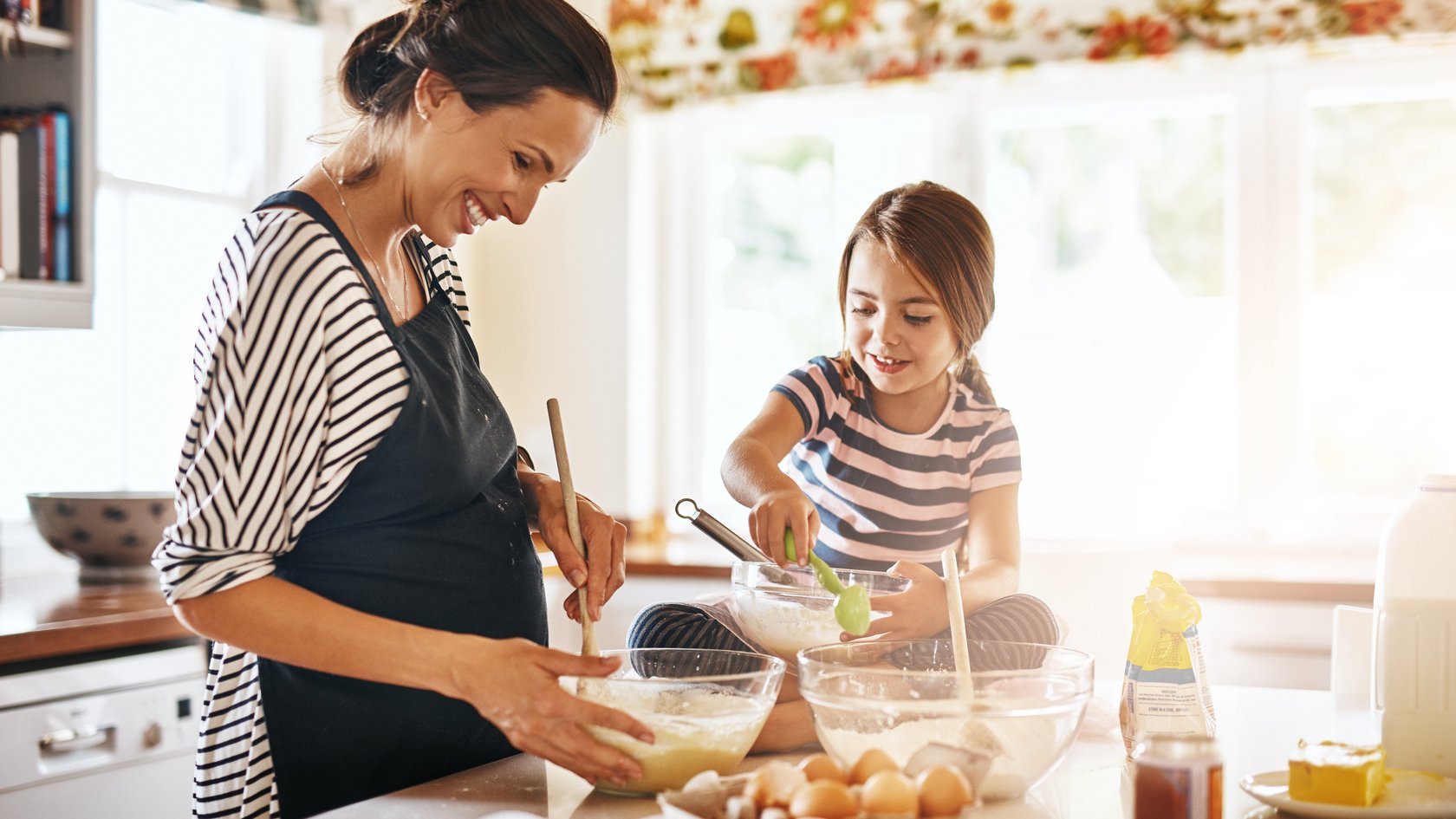 Eine Frau mit Schürze backt zusammen mit einem Mädchen einen Kuchen