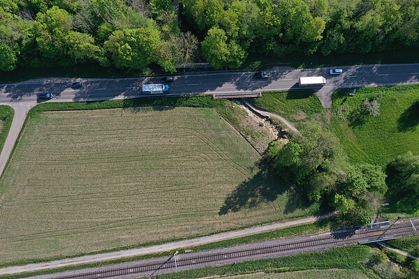 Luftbild Luftbild einer Straße neben einem Feld. Die Straße überbrückt einen kleinen Bach mit einer kurzen Brücke.