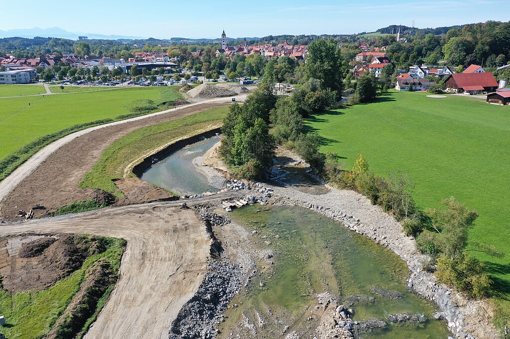 Blick von oben auf den Fluss Argen im Abschnitt 1. Man sieht den geschwungenen Verlauf mit Kiesflächen und Auelandschaft. Im Hintergrund ist die Stadt Wangen zu sehen.