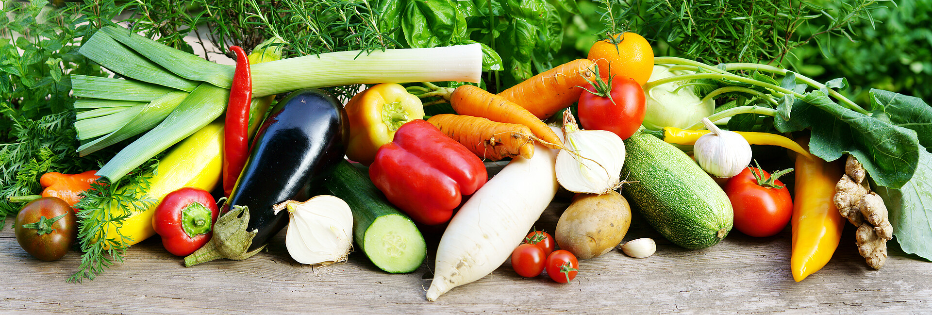 Sommergemüse (Tomaten, Zucchini, Karotten, Lauch, Paprika, Gurken) und Kräuter im Hintergrund