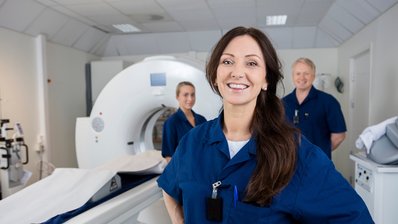 Weibliche Radiologin steht mit Kollegen vor einem MRI-Gerät
