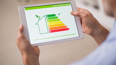 Symbolbild Gebäudeenergieeffizienz; Ein Mann hat ein Tablet in der Hand, auf dem ein Gebäude mit Energielabel zu sehen ist.