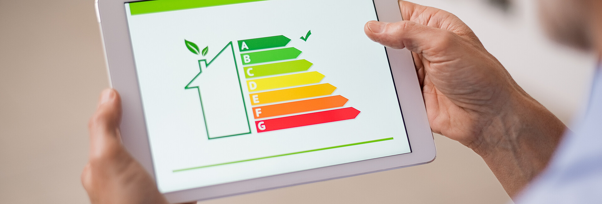 Symbolbild Gebäudeenergieeffizienz; Ein Mann hat ein Tablet in der Hand, auf dem ein Gebäude mit Energielabel zu sehen ist.