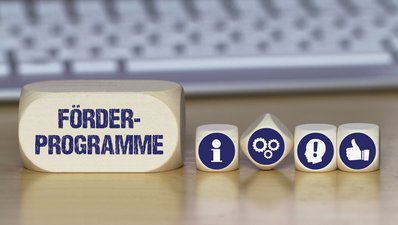 Verschiedene Würfel mit Symbolbildern für Idee, Information, Daumen nach oben und mit dem Schriftzug Förderprogramme