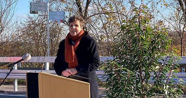 Die Regierungspräsidentin steht auf einer Brücke hinter einem Rednerpult mit Mikrofon. 