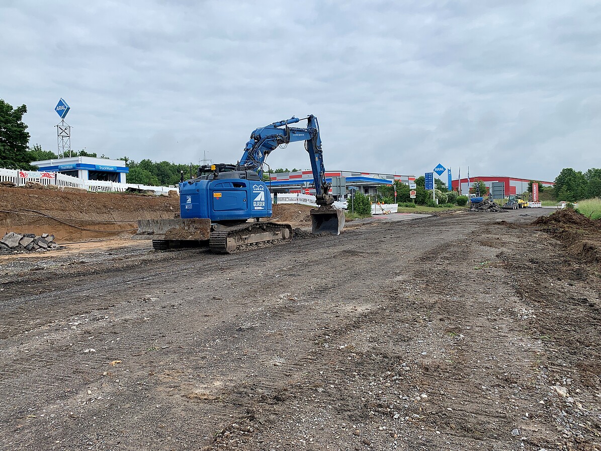Ein Bagger bei der Arbeit auf der Baustelle, im Hintergrund eine Tankstelle