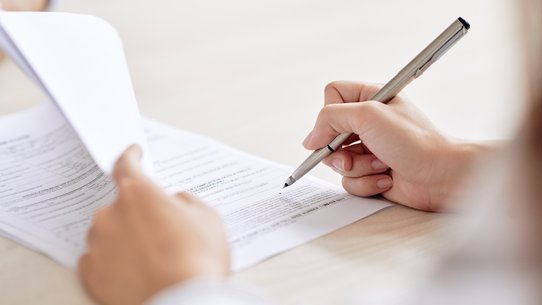 Person unterzeichnet einen Vertrag auf dem Schreibtisch