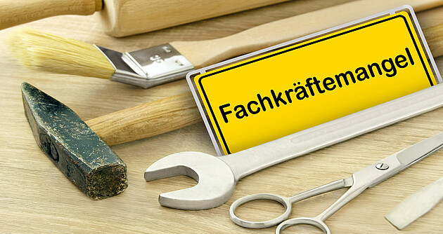 Fachkräftemangel in Deutschland Gelbes Schild und Fachkräftemangel in Deutschland mit Werkzeug auf Holz