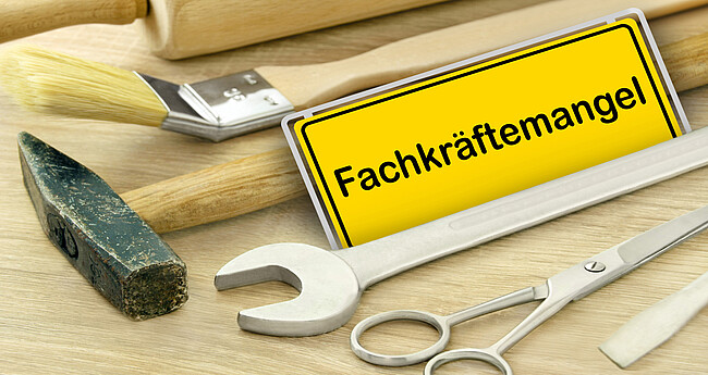 Gelbes Schild und Fachkräftemangel in Deutschland mit Werkzeug auf Holz