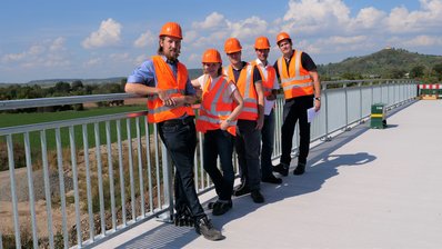 Referendare des Dualen Studiengangs "Bachelor of Engineering" stehen in Reihe hintereinander am Brückengeländer und lächeln in die Kamera