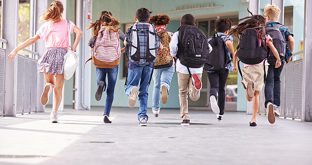 Gruppe von Grundschulkindern, die in die Schule laufen, Rückansicht