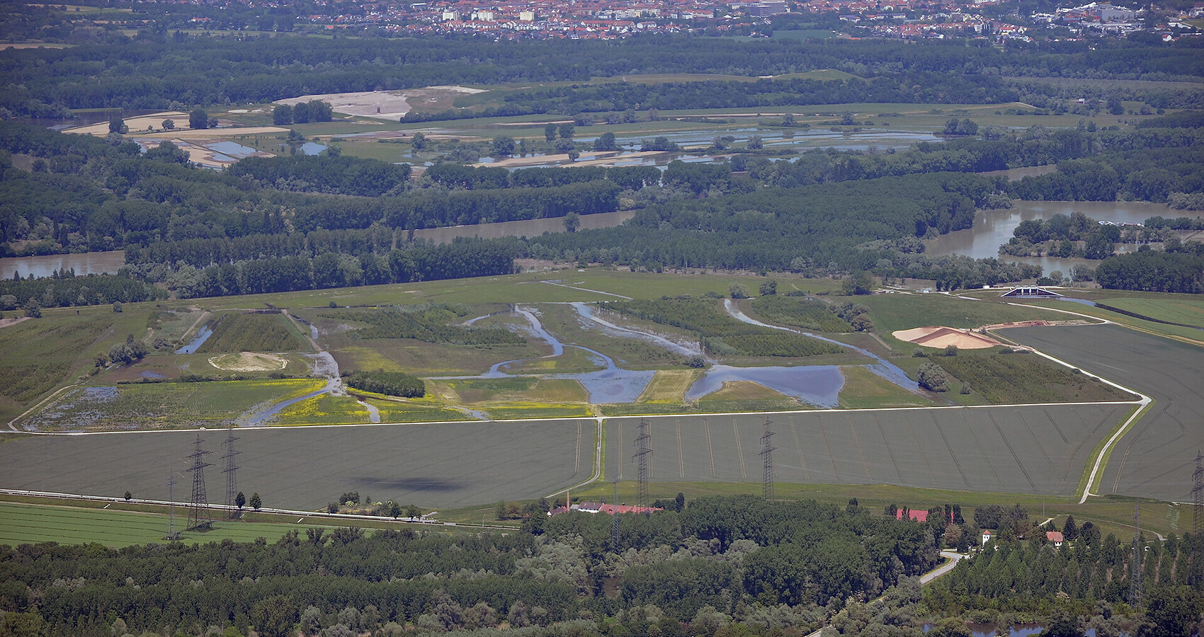 Luftbildaufnahme des Polder Rheinschanzinsel mit Blick in Richtung Norden. Zu sehen sind die mit Wasser gefüllten Gräben und Schluten im Bereich der Fläche für die partiellen Flutungen zur Auenrenaturierung. Im Hintergrund ist das überflutete Rheinvorland und auf der gegenüberliegenden Seite des Rheins der Polder Mechtersheim zu sehen.