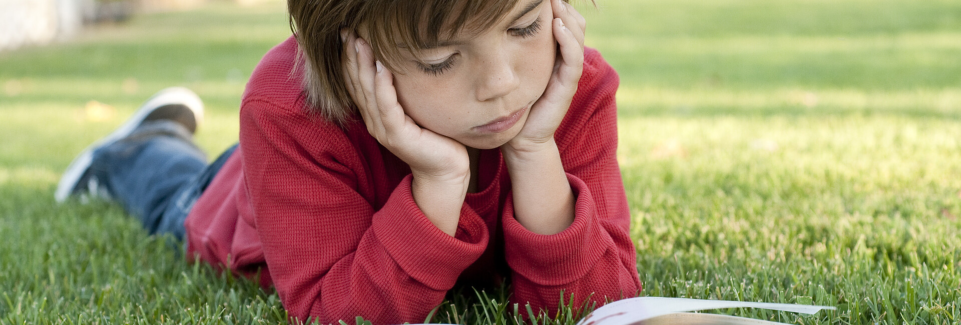 Ein Kind liest auf einer Wiese ein Buch