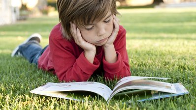 Ein Kind liest auf einer Wiese ein Buch