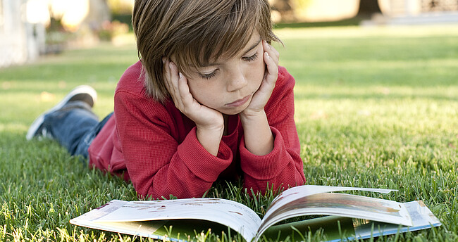 Ein Kind liest auf einer Wiese ein Buch