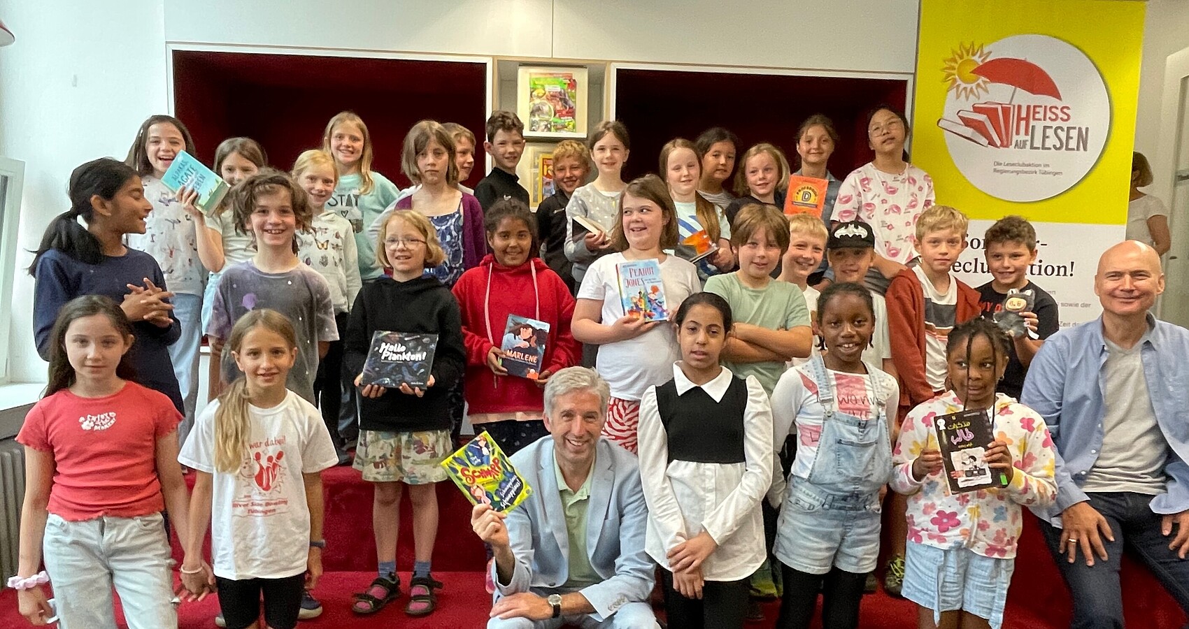 Gruppenfoto bei der Auftaktveranstaltung HEISS AUF LESEN© 2025. Mehrere Kinder und vorne in der Mitte Herr Boris Palmer (Oberbürgermeister der Stadt Tübingen) sowie vorne rechts Herr Oliver Steller (Künstler)